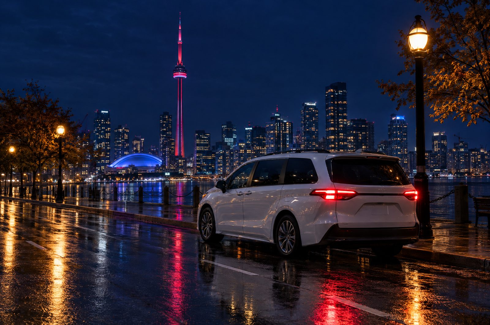 A white minivan waiting on a downtown Toronto street at night with the CN Tower behind